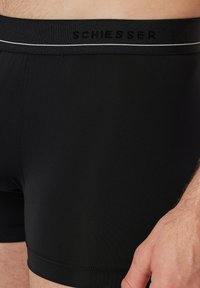 Schwarze Boxershorts aus glattem, dehnbarem Stoff, mit einem Bund, auf dem der Markenname "Schiesser" in Schwarz steht, akzentuiert durch einen weißen Streifen.