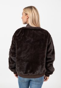 Bruine nep-bontjas met een zachte textuur, losse pasvorm en geribbelde manchetten. Bevat een bruine zoom en een eenvoudig, strak ontwerp.