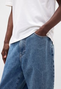 Jeans hlače iz svetlo modrega jeansa z ohlapnim krojem, natančnim zgornjim šivom in pet žepno zasnovo. Kombinirane z enostavno belo majico s kratkimi rokavi.