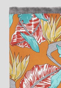 Intensywnie pomarańczowa tkanina z dużymi tropikalnymi liśćmi w kolorze czerwonym, turkusowym i żółtym, z szarym akcentem na górze. Widoczny teksturowany wzór.