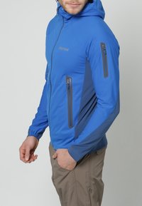 Veste isolante bleue avec capuche, dotée d'accents gris, de poches zippées et d'une coupe ajustée, fabriquée dans un matériau flexible et respirant.