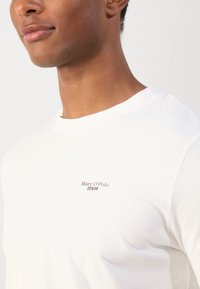 Witte katoenen T-shirt met een ronde hals, met een klein bruin logo "Marc O’Polo DENIM" op de linkerkant van de borst. Glad oppervlak.