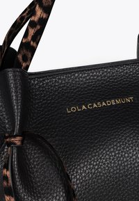 Black textured handbag with gold "LOLA CASADEMUNT" logo, featuring a leopard print strap.