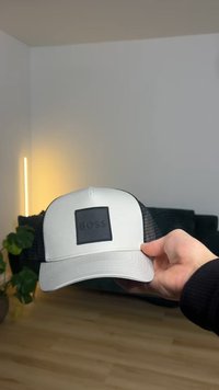 Casquette grise et noire au design structuré de baseball, avec un patch carré noir portant l'inscription "BOSS", et un dos en mesh pour la ventilation.