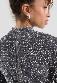 Grau glitzerndes Kleidungsstück mit hohem Kragen und Reißverschlussverschluss auf der Rückseite, das mit reflektierenden runden Pailletten bedeckt ist.