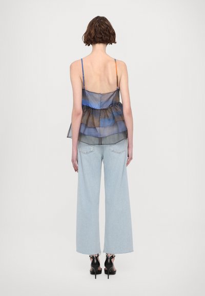 Gjennomsiktig blå og brun lagdelt topp med tynne stropper, kombinert med lyseblå vide jeans og svarte hæl sandaler. Vist fra bak.