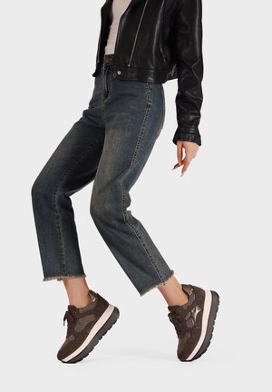 Sneaker in suede marrone con suola chunky bianca e nera, caratterizzate da dettagli metallici e un design testurizzato.