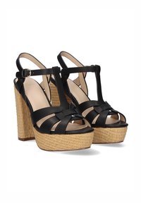 Sandalias de plataforma negras con base de paja trenzada, amplias correas cruzadas y hebilla en el tobillo. Textura de cuero suave y diseño de punta abierta.