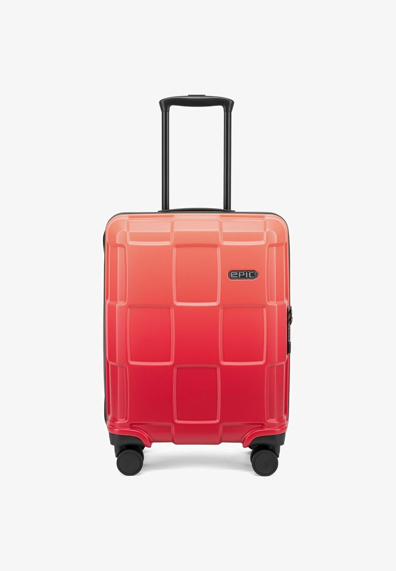 Valigia rigida in gradiente da corallo a rosso, con una texture a griglia, zip nera e ruote per il trasporto. Manico retrattile.