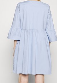 Hellblaues Baumwollkleid mit rundem Ausschnitt, dreiviertellangen Glockenärmeln und gerafftem Taillenbereich, das eine entspannte A-Linie-Silhouette zeigt.