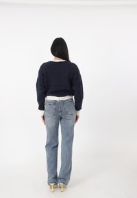Maglione navy con texture e polsini bianchi, abbinato a jeans chiari a vita alta e décolleté beige, visto da dietro.