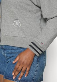 Szary sweatshirt z haftowanym logo "TH NY", z prążkowanymi mankietami z czarnymi paskami i miękką tkaniną, w połączeniu z dżinsowymi szortami.