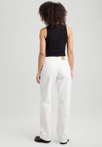 Black ribbed sleeveless top paired with loose-fitting white denim pants. Notable details include a leather tag on the waistband and chunky black shoes.