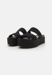 Black platform sandals with wide, soft straps and a solid, textured sole. The shoe features a thick, elevated base for added height.
