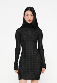 Μαύρο φόρεμα με μακριά μανίκια, εφαρμοστή σιλουέτα, υφασμάτινο σχέδιο καρό, υψηλό λαιμό και λεπτομέρεια με κυματιστό τελείωμα.