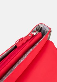 Czerwona torebka wykonana z gładkiego materiału, z zamkiem błyskawicznym, szarym wykończeniem wewnętrznym oraz eleganckim prostok�ątnym kształtem bez widocznych wzorów.