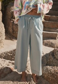 Helle blaue, weit geschnittene Strandhose mit elastischem Bund und Kordelzug, die eine glatte Textur aufweist und bis zur Mitte der Wade reicht.