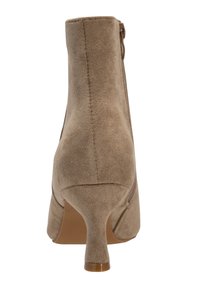 Botín de ante beige con tacón afilado, cremallera trasera, textura suave y líneas limpias, diseñado para una silueta ajustada.