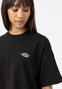 Black cotton t-shirt with short sleeves and a rounded neckline, featuring a white embroidered "Dickies" logo on the left chest area.