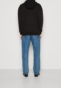 Felpa nera con cappuccio abbinata a jeans blu larghi in denim. Il tessuto sembra morbido e i jeans presentano un classico design a cinque tasche.