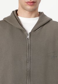 Gray zip-up hoodie made of soft fabric, featuring a hood, front zipper, and subtle branding on the chest area.