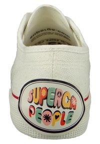 Białe płócienne trampki o teksturowanej powierzchni, z dużym, kolorowym logo "SUPERGA PEOPLE" na pięcie oraz czerwoną smugą wzdłuż podeszwy.