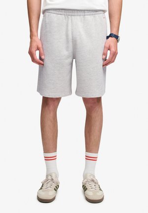 Mand iført lysegrå shorts med elastisk talje, hvide sokker med røde striber og beige sneakers med mørke striber.