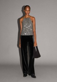 Trblietavé strieborné tielko s tenkými ramienkami, kombinované s čiernymi zamatovými širokými nohavicami a malou čiernou kabelkou. Hladké, reflexné textúry.