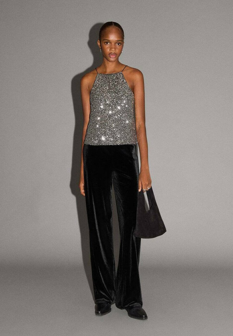 Trblietavé strieborné tielko s tenkými ramienkami, kombinované s čiernymi zamatovými širokými nohavicami a malou čiernou kabelkou. Hladké, reflexné textúry.