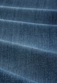Denim tkanina u tamnoplavoj boji s teksturiranom površinom i vidljivim uzorkom tkanja, koja sadrži suptilne varijacije u nijansi i završnoj obradi.