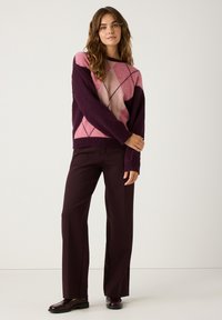 Paarse en roze argyle-gebreide trui met lange mouwen, gecombineerd met donker bordeaux brede broek en bijpassende schoenen.