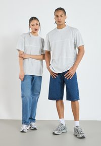 Grå, kortermede T-skjorter brukt sammen med blå denim jeans og shorts. Settet har en avslappet passform og en enkel design. Brukt med joggesko.