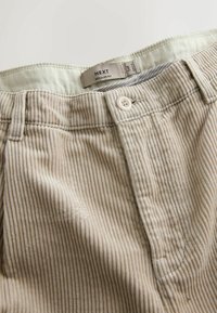 Beige corduroy trousers with subtle vertical stripes, featuring a button closure, belt loops, and a label reading "NEXT REGULAR FIT."
