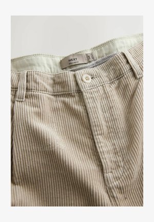 Beige kordflöjtsbyxor med subtila vertikala ränder, med knappstängning, bältesöglor och en etikett som säger "NEXT REGULAR FIT."