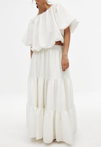 Completo bianco a due pezzi composto da un top strutturato senza spalline con maniche ampie e una gonna a strati con elastico in vita.