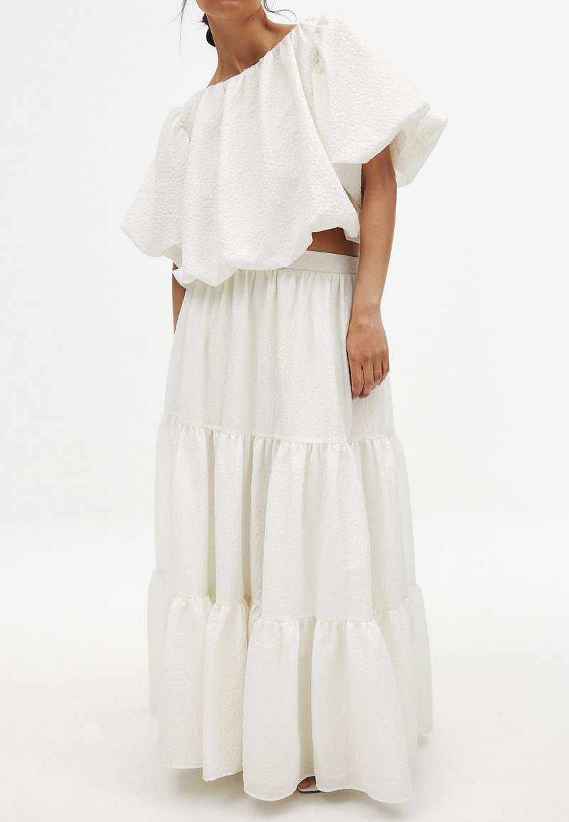 Completo bianco a due pezzi composto da un top strutturato senza spalline con maniche ampie e una gonna a strati con elastico in vita.