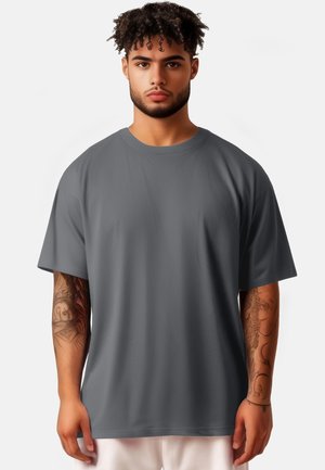 T-shirt grigio oversize con maniche corte, scollo tondo e texture liscia. Il modello ha tatuaggi visibili sugli avambracci.