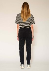 Pantalon en velours côtelé noir avec une coupe droite, associé à une chemise à rayures à manches courtes. Les chaussures présentent des accents argentés.