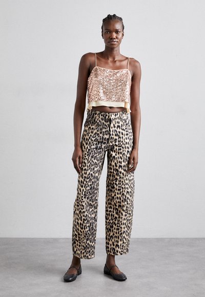 Top cropped de lantejoulas em rosa dourado com bainha de cetim; calças largas em padrão de leopardo bege; sapatos pretos planos; modelo de pé contra um fundo neutro.