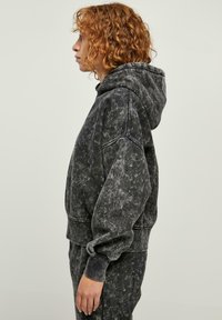 Felpa oversize grigia scura con superficie texturizzata, grande cappuccio e polsini a costine. Fa parte di un set abbinato, caratterizzato da una vestibilità morbida.