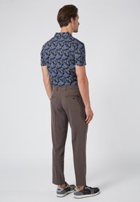 Short-sleeve floral shirt in dark blue with purple accents, paired with brown plaid trousers and black sneakers. Visible back design details.
