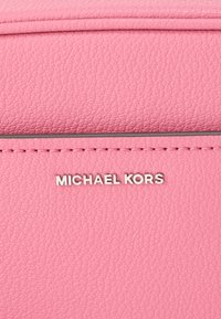 Ροζ δερμάτινη τσάντα με υφή, ασημένια στοιχεία και ανάγλυφο λογότυπο "MICHAEL KORS" στο μπροστινό μέρος.