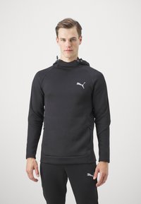 Sudadera con capucha negra de diseño ajustado, fabricada con un tejido suave. Presenta un sutil logo de Puma en gris, bolsillos frontales con cremallera y mangas texturizadas.