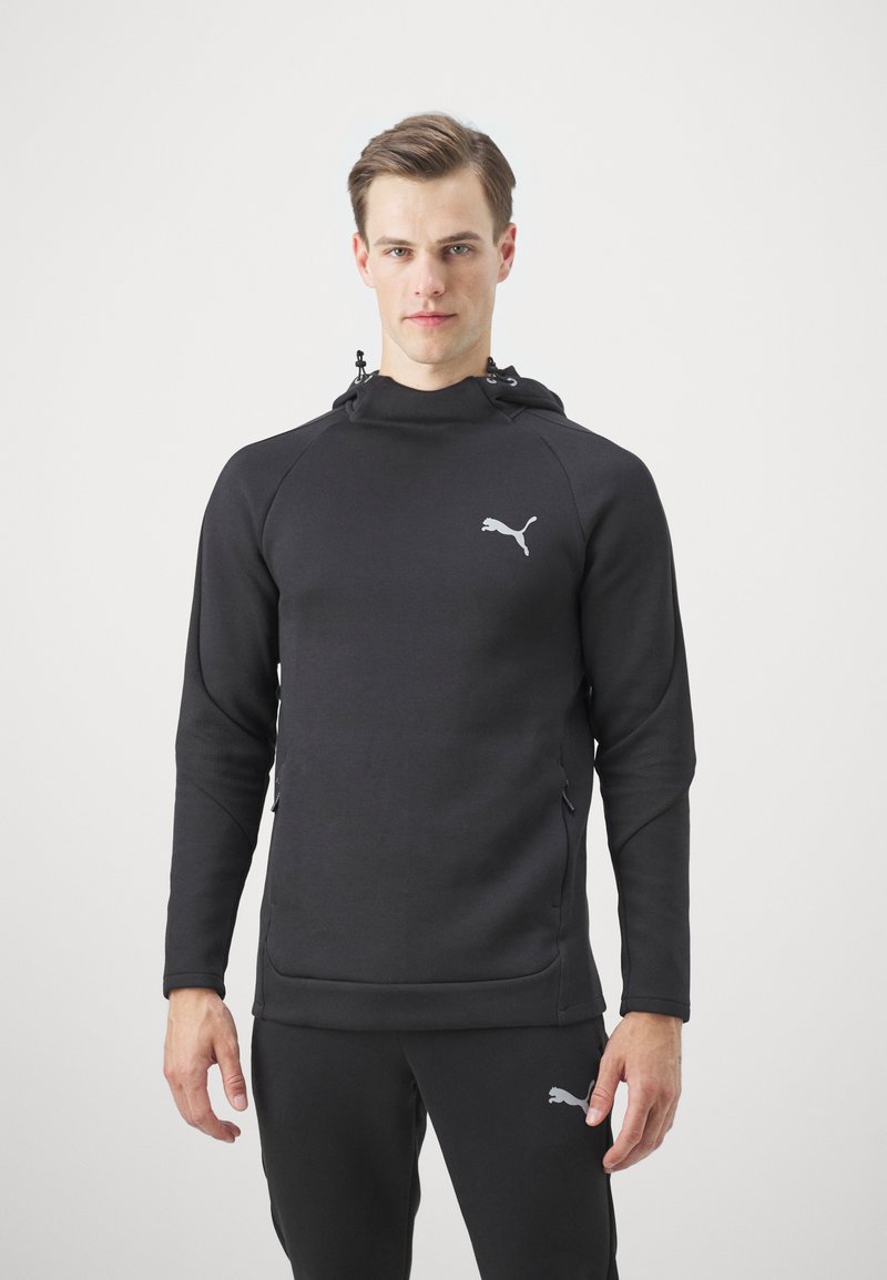Sudadera con capucha negra de diseño ajustado, fabricada con un tejido suave. Presenta un sutil logo de Puma en gris, bolsillos frontales con cremallera y mangas texturizadas.