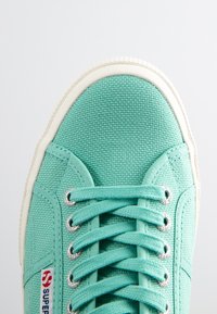 Turkusowe trampki z płótna z fakturowaną cholewką, białą gumową podeszwą, metalowymi oczkami i płaskimi sznurowadłami, z logo Super po boku.