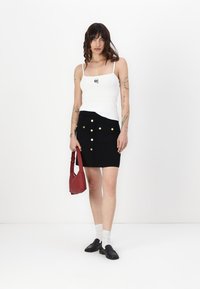 Svart mini skjørt med gullknapper, kombinert med en hvit tanktop. Tilbehør inkluderer en rød veske og svarte sko. Jevn tekstur, tettsittende design.