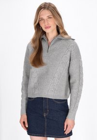 Pulover gri tricotat cu guler tip jumătate cu fermoar și detalii texturate de tricot în cablu, asortat cu o fustă mini din denim de culoare albastru închis.