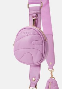 Sac bandoulière en cuir violet avec un design circulaire, logo en relief, surface texturée et quincaillerie en ton doré avec fermeture éclair.