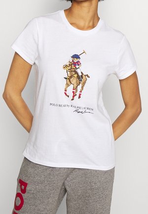 Valkoinen t-paita, jossa ristipistoin kuvattu hevosella ratsastava polo-pelaaja sekä teksti "POLO BEAR by RALPH LAUREN", yhdistetty harmaisiin collegehousuihin.