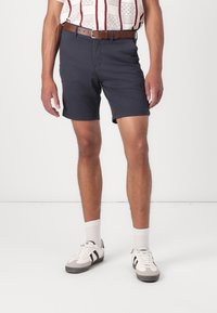 Marineblauwe shorts met een gladde textuur, voorzien van een voornaad, riemlussen en een klassieke snit. Gecombineerd met witte sneakers en sokken.